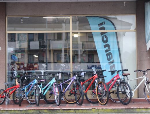 Vetrina di Cicli Girelli con esposizione di biciclette nuove di diversi colori e modelli, inclusa una bandiera Bianchi. Servizi di vendita e riparazione biciclette.