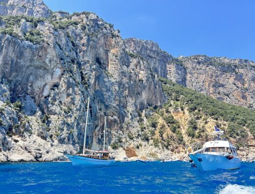 Cielomar Noleggio Gommoni Cala Gonone: due imbarcazioni turistiche ormeggiate in mare con scogliera sullo sfondo a Cala Gonone, Sardegna.