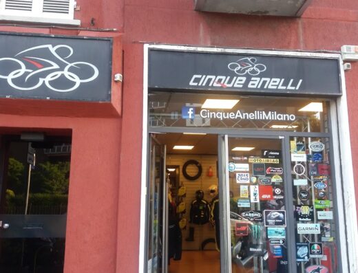 Foto del negozio Cinque Anelli a Milano, specializzato in accessori e abbigliamento per motociclisti e viaggi in moto. Vetrina con adesivi di marchi noti.