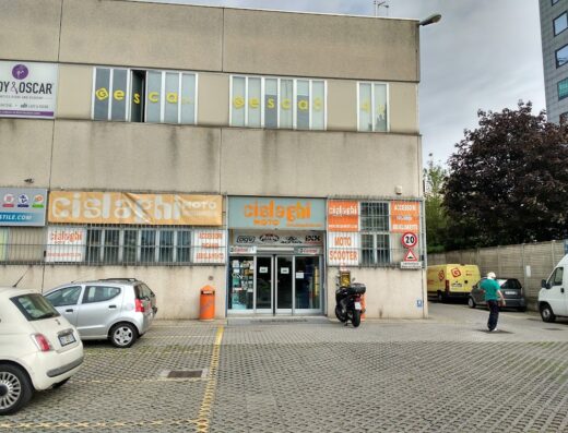 Cislaghi Moto: negozio di ricambi e accessori moto con insegna ben visibile, parcheggio con auto e moto, e indicazioni stradali.