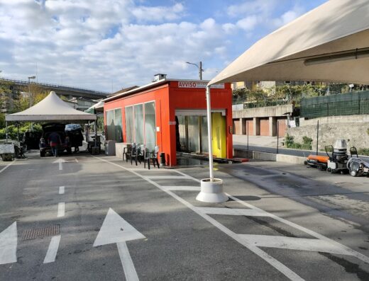Autolavaggio Clean Cars: vista esterna dell'autolavaggio con auto in fase di pulizia, zona d'attesa coperta e attrezzature per la pulizia.