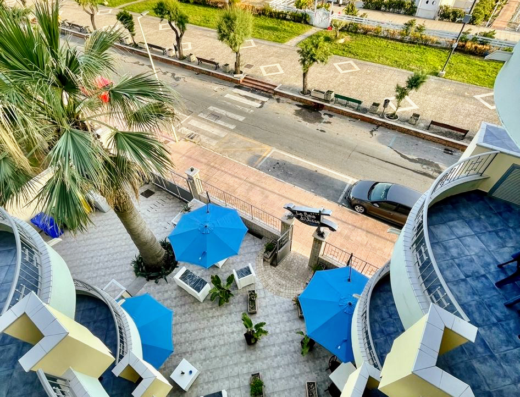 Vista aerea del Club Vacanze La Baia di Ulisse con ombrelloni blu, arredi esterni e la spiaggia in lontananza.