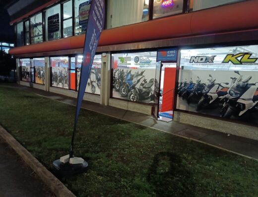 Concessionario CMTmotor Torino con vetrine espositive di moto e scooter. Vetrina con esposizione di veicoli elettrici, cartello aperto e bandiera CMT motor.