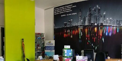 Interno di un'agenzia di viaggi CNG Travel con una mappa del mondo appesa al muro, un muro verde acceso, poster di Costa Crociere, uno sfondo con la skyline di una città e decorazioni.