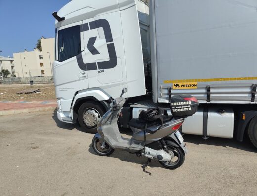 Scooter grigio parcheggiato di fronte a un camion bianco. Bauletto portaoggetti "Noleggio Scooter" visibile. Colaci Moto di Adolfo Colaci.