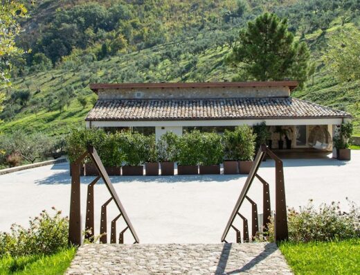 Colle Serrano Relais Resort vista esterna con vegetazione, vialetto in pietra e collina verde sullo sfondo, architettura tipica italiana.