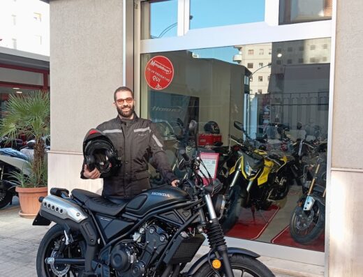 Un cliente sorridente posa con una Honda Rebel 500 nera di fronte alla concessionaria Honda Moto Cometa, tenendo in mano il casco.