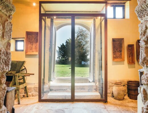 Interno del Convento San Bartolomeo dimora storica con vista sull'esterno attraverso una porta vetrata, elementi di arredo rustico e mura in pietra.