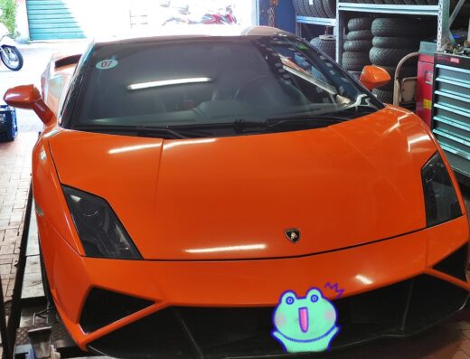 Orange Lamborghini being serviced in a garage, possibly for tire assistance or maintenance. Car accessories and tools are visible.