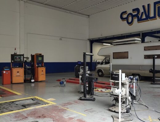 Interno di un'officina Corauto revisioni con attrezzatura per la manutenzione di auto e camper, inclusi analizzatori e ponte sollevatore.