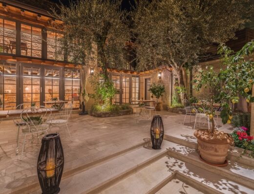 Corte Alma Spa and Luxury Home: Elegante patio esterno con tavoli e sedie in ferro battuto, illuminato da lanterne e alberi di ulivo, per un'esperienza di lusso e relax.