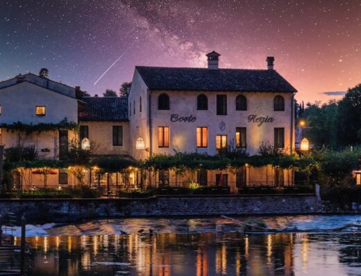 Corte Regia Relais illuminato di notte, con cielo stellato e riflessi sull'acqua, atmosfera romantica e suggestiva, location turistica