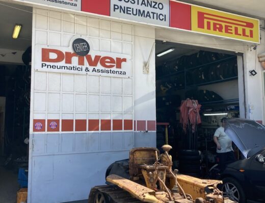 Costanzo Pneumatici SNC Driver Center Pirelli: officina di pneumatici con insegne Driver e Pirelli, un trattore cingolato d'epoca e auto in riparazione.