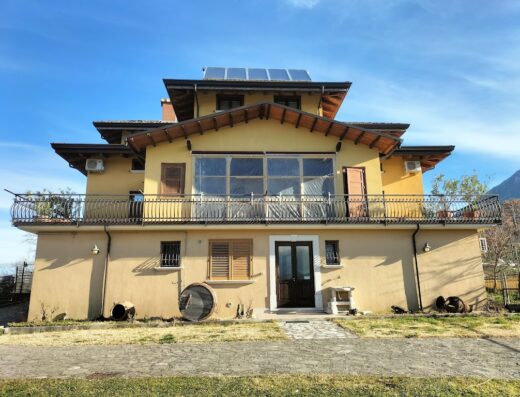 Country House Nonna Pina Di Belingo Pascal: A two-story yellow country house with a balcony, red tile roof, and solar panels under a blue sky.
