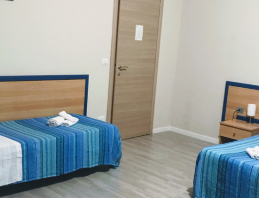 Interno di Country House Paola con tre letti singoli, biancheria blu a righe e asciugamani bianchi, comodino con lampada e porta in legno sullo sfondo.