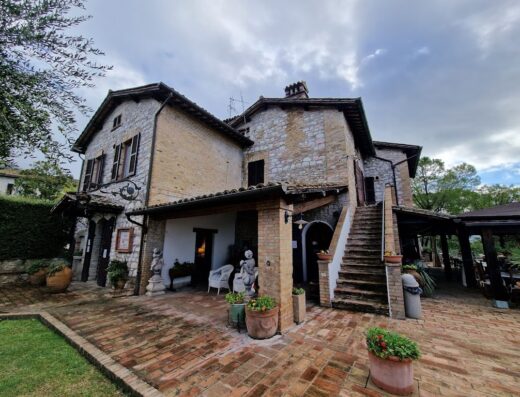 Esterno della Country House Tre Esse, con facciata in pietra, mattoni, patio in laterizio, sculture decorative e vegetazione rigogliosa.