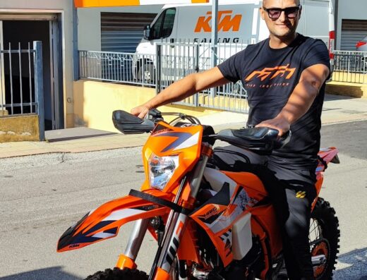 Un uomo su una moto KTM arancione davanti a un negozio di moto Coven Bike Sas Di Briganti, con furgone e insegna MAC visibili sullo sfondo.