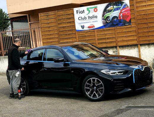 Un uomo sta lucidando una BMW nera in un autolavaggio. Sullo sfondo, un cartello del Fiat 500 Club Italia.