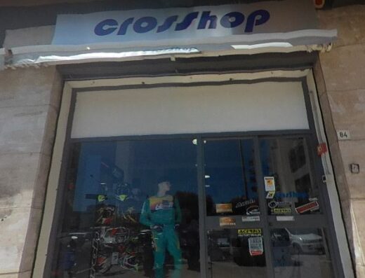 La vetrina del negozio Crosshop mostra una moto da cross e un manichino con abbigliamento da motocross, evidenziando accessori e servizi per appassionati di moto.