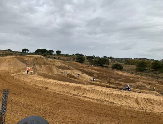 Crossodromo S. M. MOTO Park: Vista panoramica del circuito di motocross con piloti in azione, terreno sabbioso e cielo nuvoloso. Moto e sport estremi.