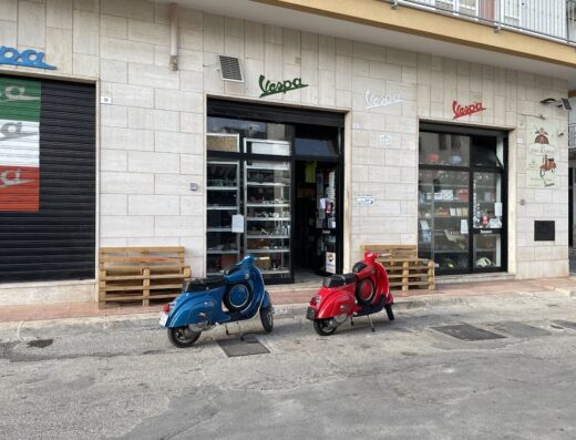 Da Zio Mario: negozio di ricambi e accessori per Vespa con due scooter Vespa blu e rossa parcheggiate di fronte.