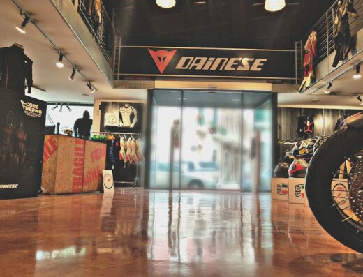 Interno del negozio Dainese con abbigliamento e accessori moto, tra cui tute, caschi AGV e pneumatici in esposizione.