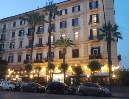 Edificio a più piani con balconi e palme a Napoli, Italia, vicino alla Dalla Vecchia Pneumatici S.r.l., illuminato di sera.