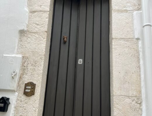 Ingresso caratteristico in pietra bianca e porta in legno scuro del Dama Bianca Boutique Hotel a Ostuni, Puglia, Italia.