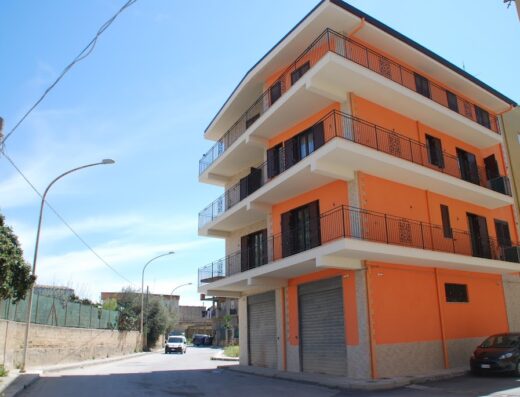 Daphnae House: Facciata colorata di un edificio a più piani con balconi, situato in una strada tranquilla con auto parcheggiate e un cielo azzurro.