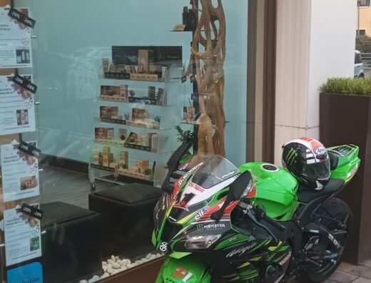 Una moto sportiva verde Kawasaki parcheggiata davanti a "Waikiki Estetica & Solarium", con casco sul sedile. Accessori moto e negozio di bellezza.
