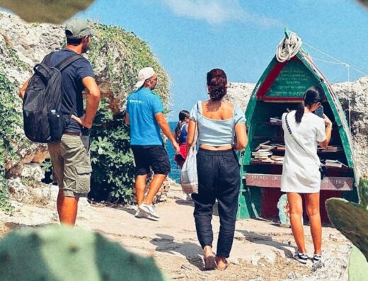 People visiting a unique outdoor library shaped like a boat in Puglia. The scene shows tourists enjoying the coastal landscape and cultural attractions of the region, perfect for tour promotions and travel inspiration.
