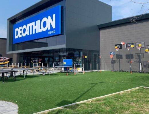 Decathlon Treviso store exterior featuring sports equipment on display, including kayaks, ping pong tables, and basketball hoops, set against a modern building facade.