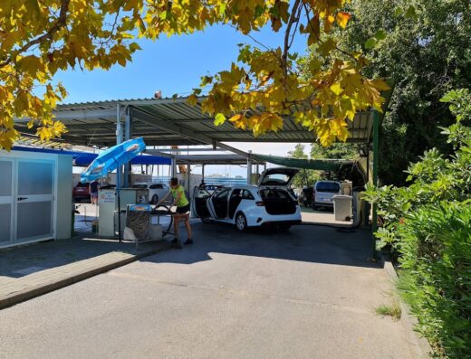 Autolavaggio self-service Del Freo con auto bianca in fase di pulizia, aspiratore in uso e tettoia protettiva.