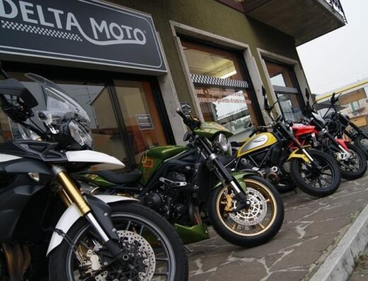 Esposizione di moto usate e nuove di fronte al negozio Delta Moto: Triumph Tiger Explorer, Street Triple e Ducati Scrambler.