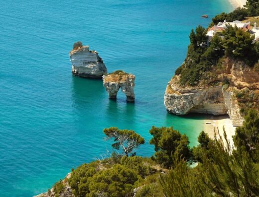 Scogliera a picco sul mare Adriatico cristallino, con faraglioni e vegetazione rigogliosa, ideale per tour in barca e scoperta delle grotte marine del Salento.