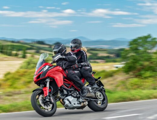 Una coppia su una moto Ducati rossa su una strada di campagna in Italia, servizio di noleggio moto DesmoRent.