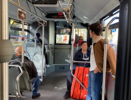 Interno di un autobus con passeggeri seduti e in piedi, segnaletica luminosa visibile, ambiente urbano.