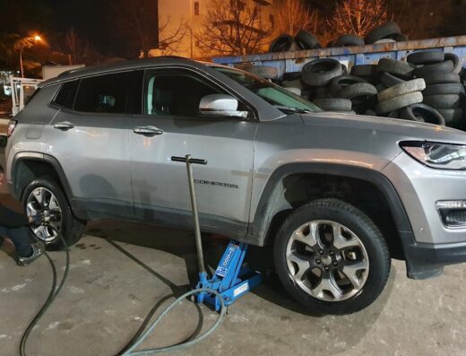 Un veicolo Jeep Compass grigio sollevato con un cric idraulico per la sostituzione pneumatici presso Di Giovanni Gomme S.A.S.