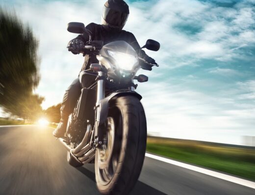 Motociclista in sella a una moto da strada, con casco integrale, che viaggia ad alta velocità su strada asfaltata con cielo azzurro. Dieffe Moto di Gaiga Fabio: vendita e assistenza moto e scooter.