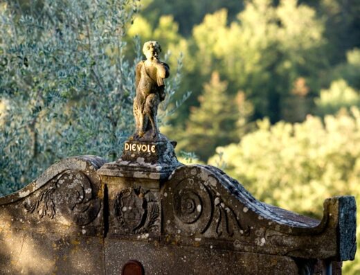 Scultura in pietra con la scritta 'Dievole' presso il Dievole Wine Resort, con sfondo di alberi verdi.