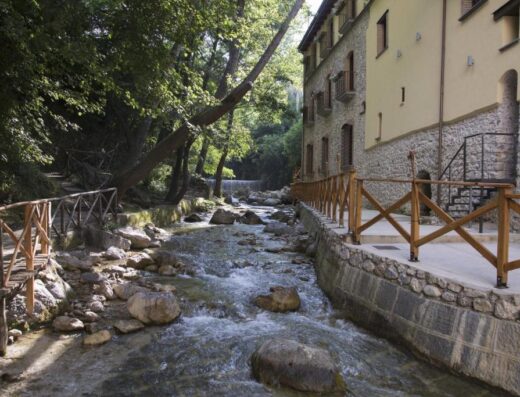 Dimora Storica Maccarunera: Scenic view of a historic building nestled beside a flowing river, complete with wooden bridges and natural stone architecture.