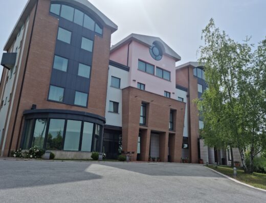 Architettura moderna con facciata in mattoni rossi e dettagli rosa, ampie finestre e design contemporaneo, illuminata dalla luce solare.