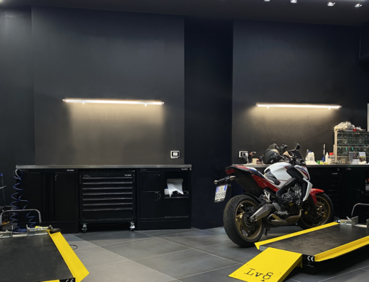 Interno di Dr.ive Scooter Clinic, centro assistenza e riparazione scooter: moto bianca e rossa su ponte sollevatore, attrezzatura professionale per riparazioni.
