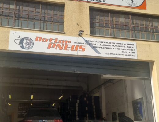 Dr. Pneus: Vendita pneumatici auto e moto. Immagine dell'officina con auto sul ponte sollevatore, scooter parcheggiato e personale al lavoro sui pneumatici. Servizi professionali per la tua moto e auto.