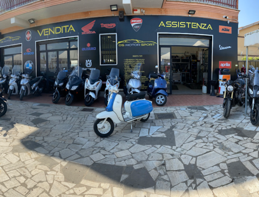 DS Motorsport concessionaria moto nuove e usate: esposizione di scooter e moto di vari marchi, tra cui una Lambretta d'epoca bianca e blu.