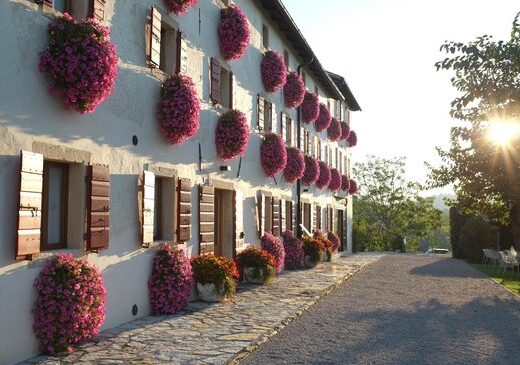 Duca di Dolle: Facciata di edificio storico con finestre adornate da fiori rosa, tipico esempio di architettura rurale italiana, situato in un paesaggio pittoresco.