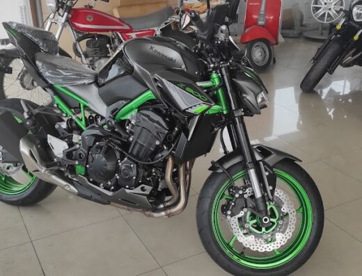 Moto Kawasaki Z900 nera e verde in esposizione, parte di un concessionario o marketplace di moto, con altre moto e scooter visibili sullo sfondo.