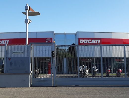 Ducati Roma concessionaria: esposizione di motociclette Ducati dietro il cancello, vetrine con logo e insegna Roma, servizio vendita e assistenza Ducati.