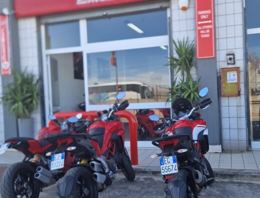 Tre motociclette Ducati rosse parcheggiate davanti a un negozio Ducati, che mostra la gamma e gli accessori disponibili per gli appassionati di moto.