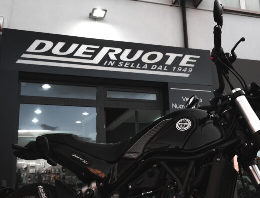 Moto Benelli Scrambler 500 nera esposta davanti al negozio Due Ruote Moto: abbigliamento e accessori per motociclisti dal 1949.